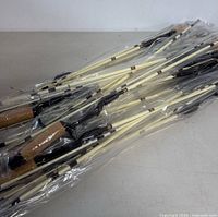 Multiple fishing rods bundled together, each individually wrapped in plastic, showing cork handles and cream-colored rod blanks.