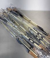 Photo showing 25 fishing rods individually wrapped in plastic bags lying flat, all with cork grip handles and similar construction.