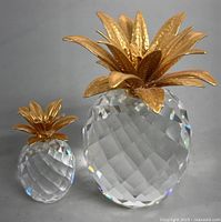 Front side view of both Swarovski crystal pineapple ornaments showing faceted crystal bodies and gold-toned hammered metal leaves