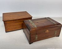 Two wooden boxes side by side on a white surface, one with metal hinges and accents, the other simpler.