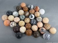 Overhead view displaying all 36 stone marbles showcasing a variety of natural colors and patterns in a loosely arranged pile.