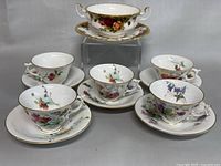 Photo showing five Royal Worcester English floral patterned teacups each with matching saucers, and one Royal Albert double handle cup with saucer, arranged to display the set.
