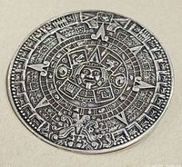 Front view of the circular silver brooch or pendant with Aztec sun calendar design showing detailed embossing of the central face and surrounding glyphs.