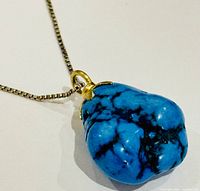 Close-up photo of the turquoise stone pendant hanging on a silver chain, showing the vibrant blue color and black matrix pattern of the stone.