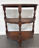 Front angled view of antique half moon wooden table showing three shelves and turned legs.