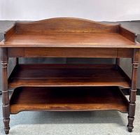 Front view of antique solid wood wash stand showing three shelves, turned legs, and raised back edge on top shelf.