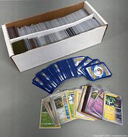 White cardboard storage box filled with Pokemon cards, fanned card backs and sample fronts.