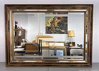 Front view of the rectangular mirror showing entire beveled glass surface and ornate gold-tone carved wooden frame with reflection of room interior.