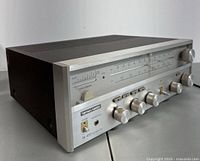 Angled front view showing brushed aluminum front panel, control knobs, and AM/FM tuner display