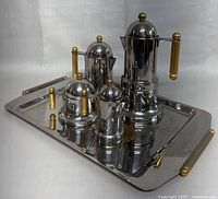 Set of five stainless steel coffee and tea vessels with gold-tone handles and finials, displayed on a matching rectangular serving tray, showing the entire coffee set together.