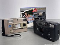 Photo showing the Polaroid OneStep AutoFocus camera in original box, Nikon AF400, and Disc7 cameras together from a side angle