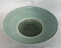 Angled view of the blue-green glazed pottery bowl showing the interior design, including the darker center and raised decorative elements
