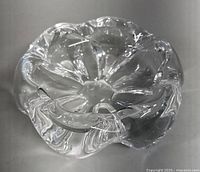 Top and angled side views of the clear heavy crystal ashtray showing its thickness, scalloped edges and internal swirls.