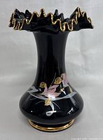 Front view of vintage black glass vase with ruffled gold-trimmed top and hand painted pink and gold floral design.