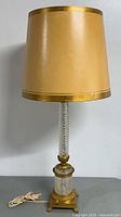 Front view of the vintage gold-toned lampshade and cut glass crystal brass lamp base with power cord shown coiled beside the lamp.