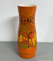 Front view of the vase showing bright orange glaze with hand-painted abstract floral design in green, yellow, and orange colors.