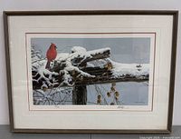 Framed artwork showing a cardinal on a snowy wooden fence, with signature and numbering visible below the image.