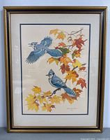 Framed lithograph print showing two blue jays on autumn leaves in a gold-toned frame with mat.