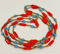 Close-up image of the long necklace showing red cylindrical beads, small turquoise beads, and gold spacer beads on a neutral surface.