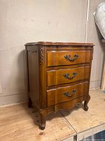 Angled view of the French Provincial nightstand showing the curved legs, carved details on the side, and front ornate drawer handles.