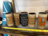 Photo showing all five Edison cylinder record containers with visible labels and wear.