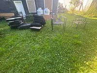 Image showing six metal patio chairs and multiple black cushions spread on grass outdoors.