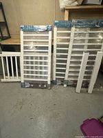 Three white vinyl railing panels wrapped in plastic, standing vertically against a wall on a concrete floor.