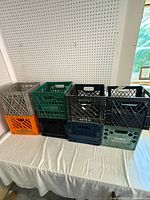 Group of 8 plastic milk crates stacked in two rows on a white tablecloth with pegboard background.