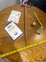 Photo showing wooden golf club trophy, souvenir golden golf ball, miniature golf club, Rules of Golf booklet and 'The Ultimate Tee' booklet on wooden table.