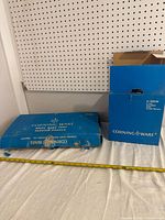 Blue worn Corning Ware boxes for broil bake tray and percolator on white surface with measuring tape for scale.