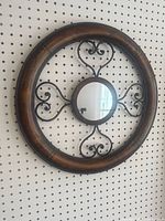 Overall view of the circular wall mirror showing the wooden outer ring and black decorative metal scroll frame with small round mirror at the center.