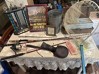 Overall fishing lot including rods, net, tackle box, and decorative sign on lace tablecloth