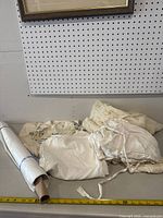 Lot of various linens spread out on table including floral embroidered fabrics, lace pieces, and plain white linens, showing overall wear from use.