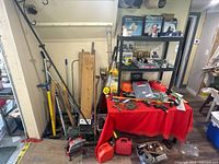Full view of metal tools, jerry cans, assorted hardware on a red table and black shelf with various items including phones and toolboxes.