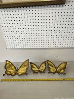 Four metal butterfly wall sculptures lined up, showing largest is about 10 inches wide, all with yellow painted wings and brown edges.