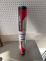 Rolled-up welcome mat in original packaging standing upright on a surface against pegboard background.