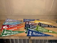 All 12 vintage felt pennants representing Canadian provinces and territories arranged on a wooden surface, showing various colors and graphics.