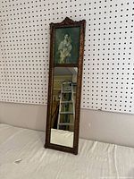 Full view of the tall, narrow ornate framed mirror leaning against wall showing upper printed image and lower mirror