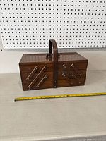 Closed view of the rectangular wooden sewing box with handle and fold-out sections.