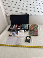 Poker chip set and multiple decks of playing cards arranged next to a tape measure for size reference.
