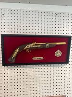 Full view of flintlock replica pistol mounted in black frame with red felt backing, including two metallic plaques.