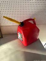 Red 20L gasoline container with yellow spout and handle, shown on pegboard shelf.