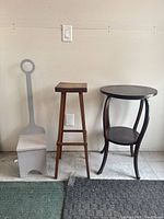 Three wooden stands/tables shown together against a wall, including a tall narrow stool, a dark brown round two-tier table, and a grey stand with a circular handle.