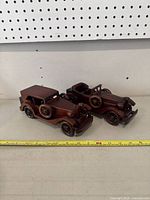 Photo showing two hand carved wooden models of vintage cars placed side by side with measuring tape indicating size.