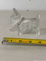Front view of clear glass Scottie dog paperweight with measuring tape showing approximately 3.5 inches length.