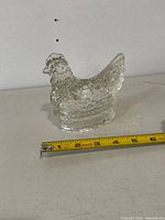 Side view of vintage glass chicken hen figurine placed on white surface with measuring tape showing nearly 3.5 inches length