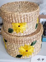 Stacked view of both round raffia baskets showing lids and yellow flower decorations
