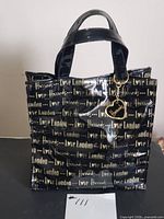 Front view of Harrods black patent tote showing gold script and charm