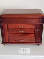 Front view of closed reddish-brown wooden jewelry chest showing four drawers and side columns