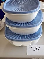Stack of three white Tupperware bowls with blue lids, showing size gradation